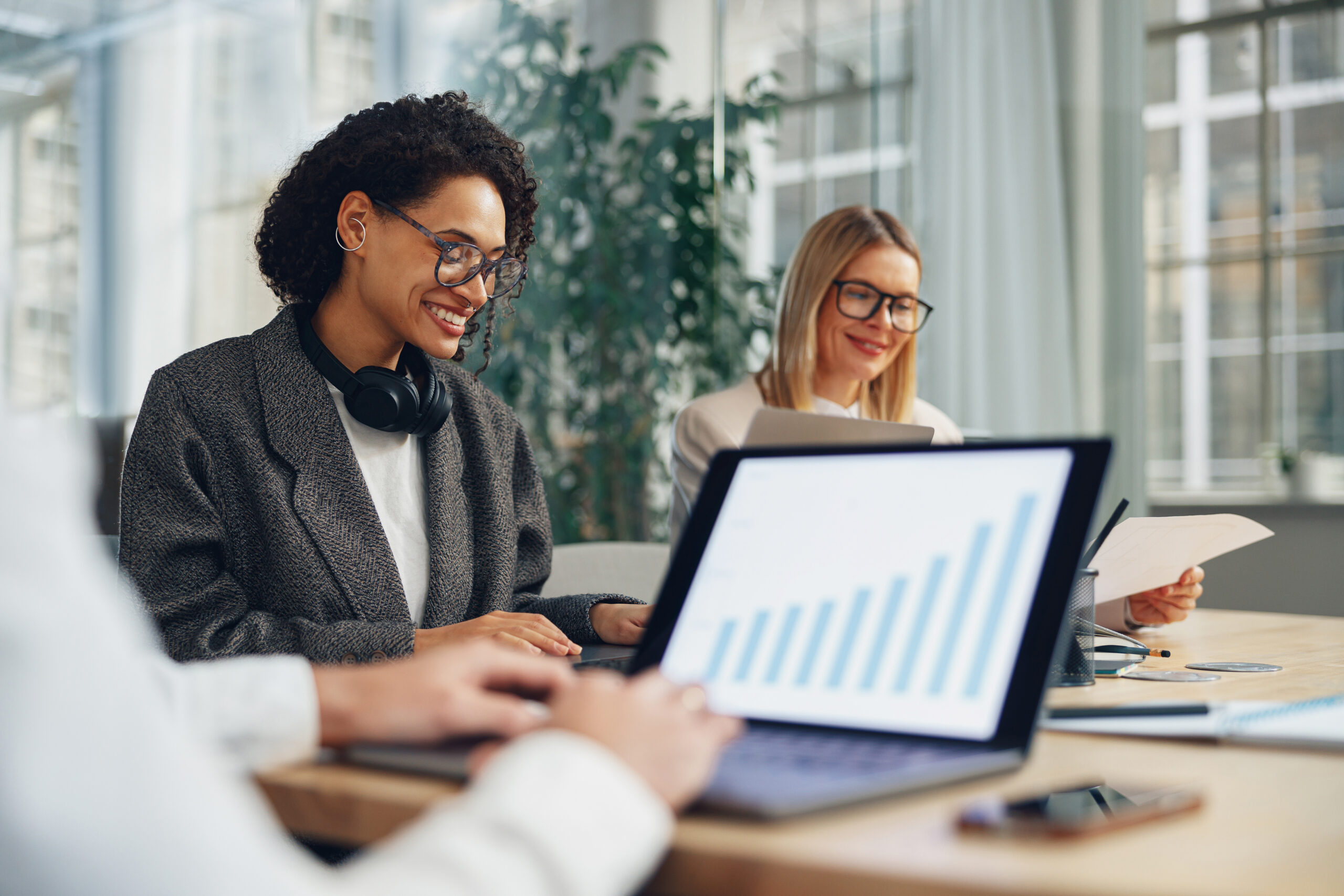 Smiling woman manager working on laptop in modern coworking while sitting near colleagues